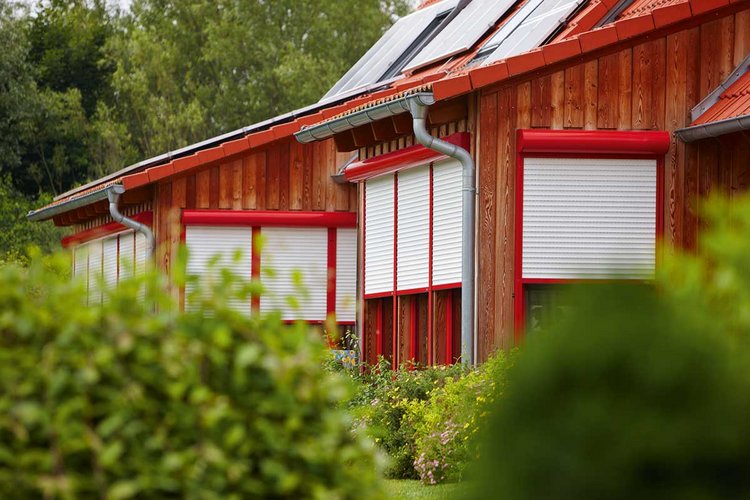 mehrere rot-weiße Rollläden an einem braunen Haus
