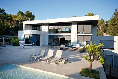 weißes Haus mit vielen Fenstern mit einem Pool und Liegestühlen im Vordergrund