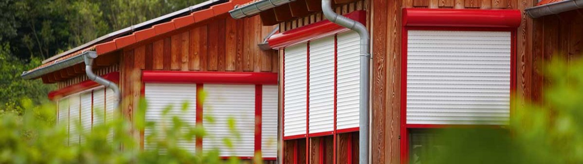 mehrere rot-weiße Rollläden an einem braunen Haus